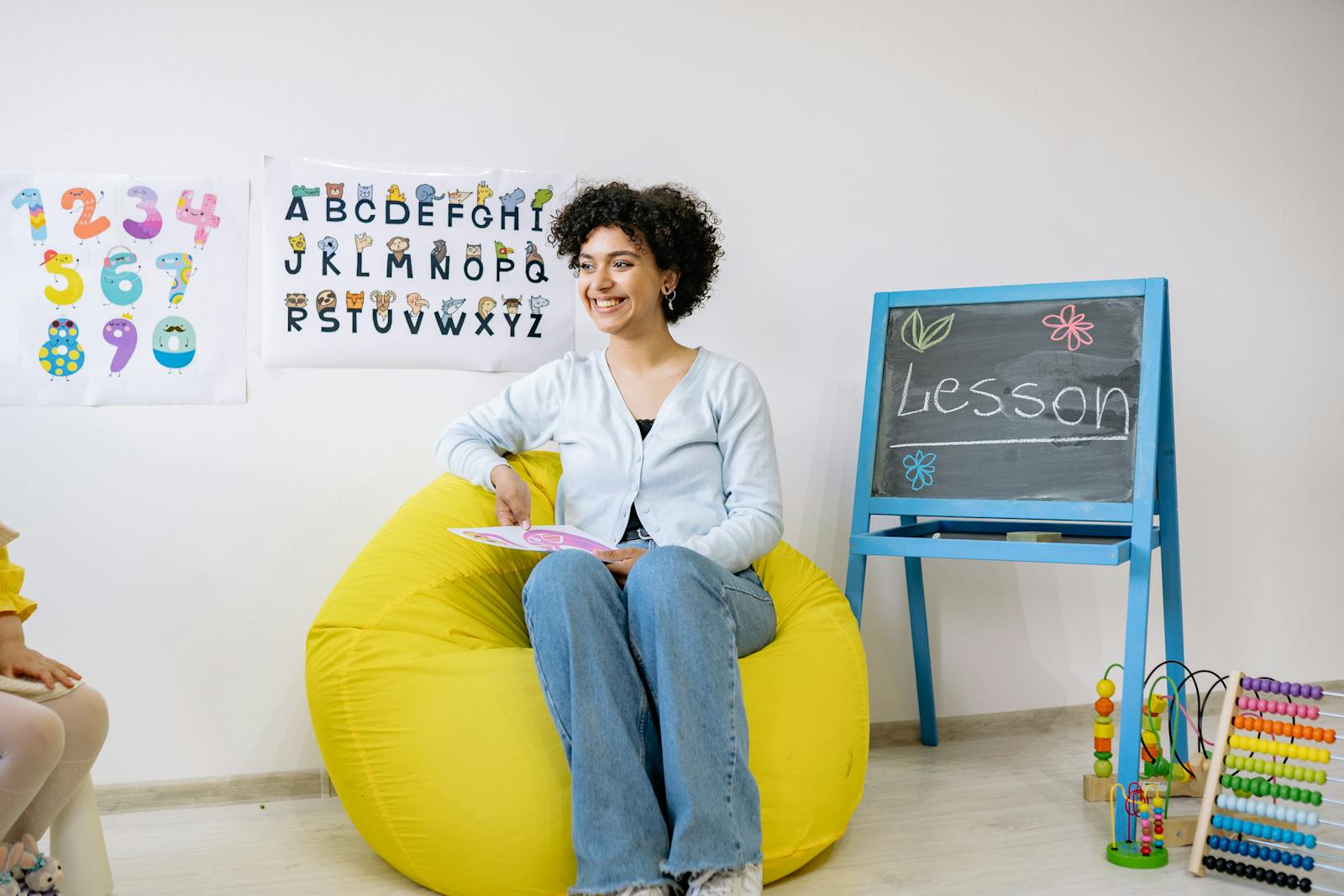 Smiling teacher sitting in a classroom, holding a book and teaching preschool students.